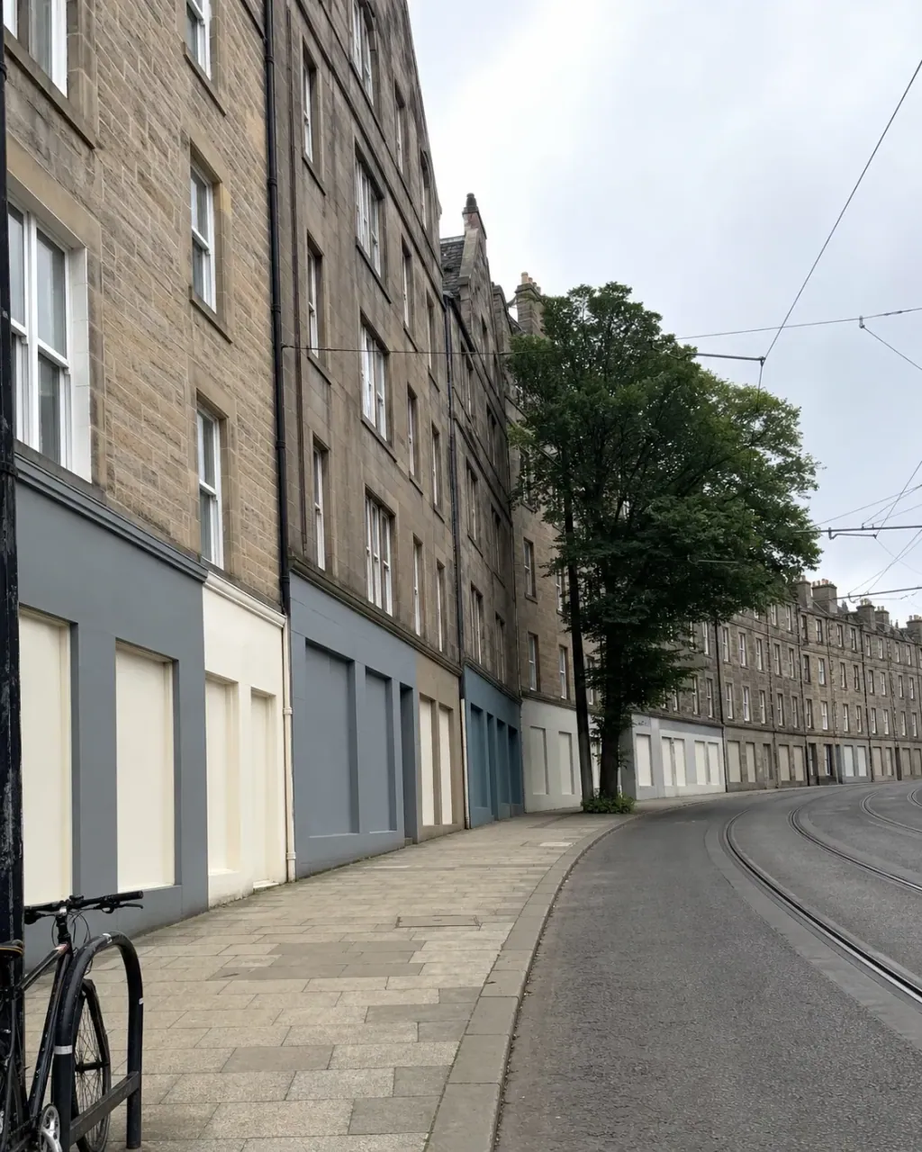 Stone tenements above painted shopfronts on Leith Walk, tram wires overhead