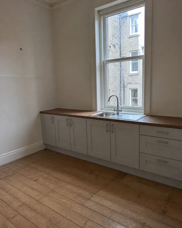 A cleaned empty tenement kitchen with a sash window and bare worktops