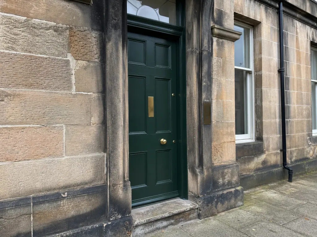 The deep green shared stair door of an Edinburgh tenement entrance