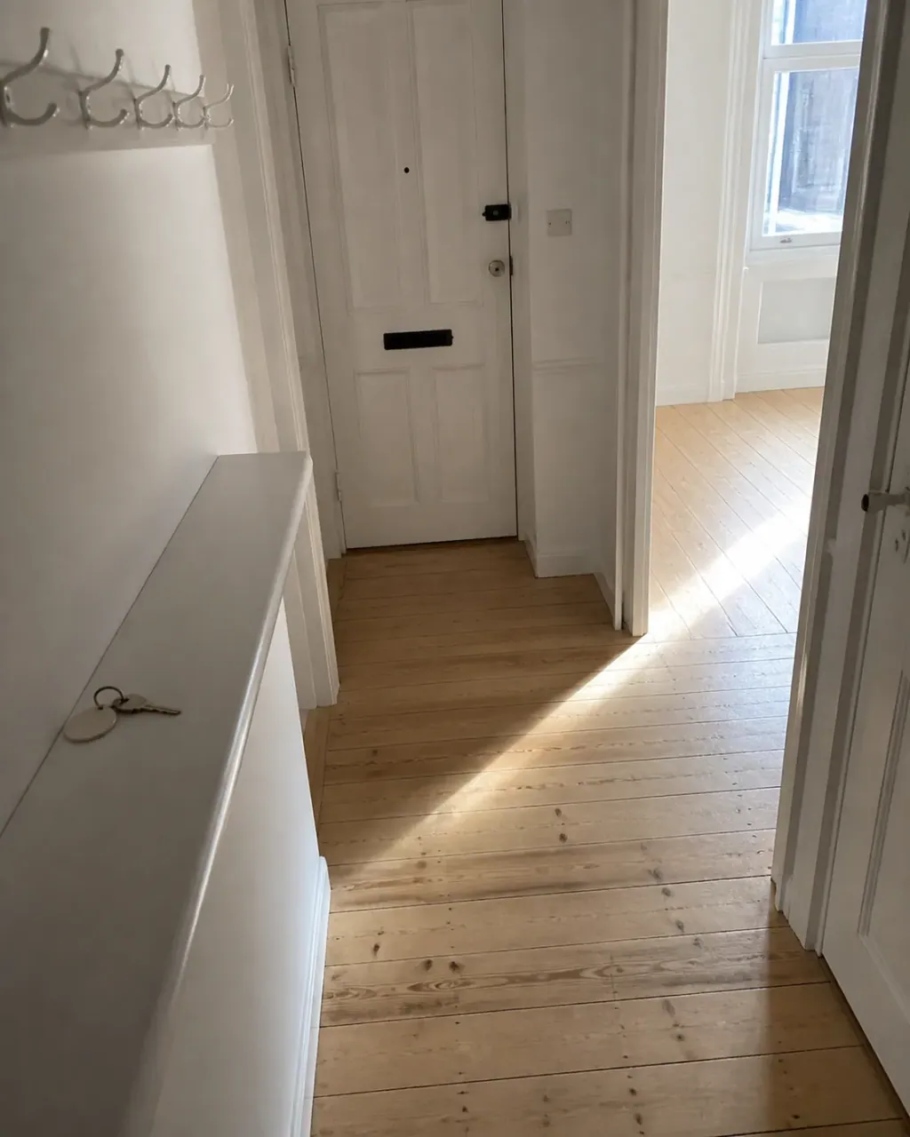 An empty flat hallway with the front door key left on the hall shelf after a checkout clean